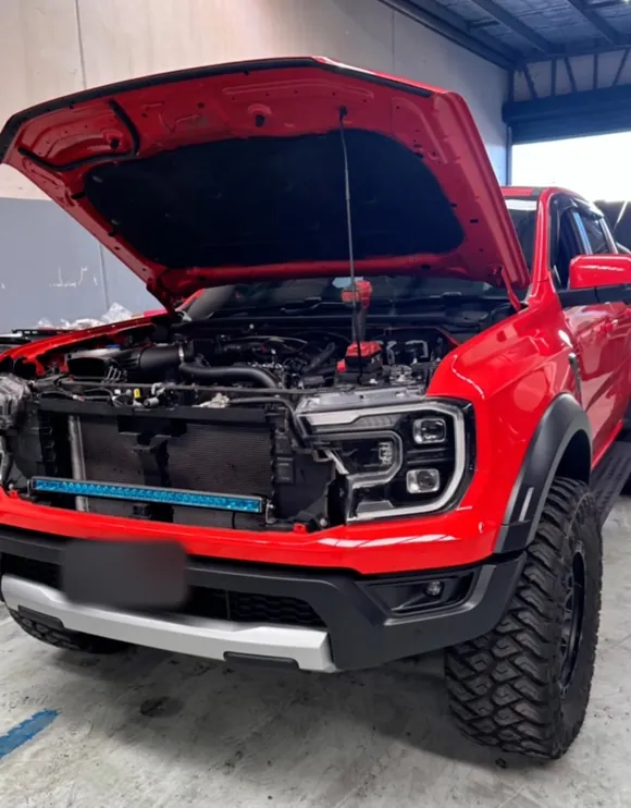 Red Ford Ranger Raptor with the bonnet up and the grille off, a slim LED light bar fitted in front of the radiator
